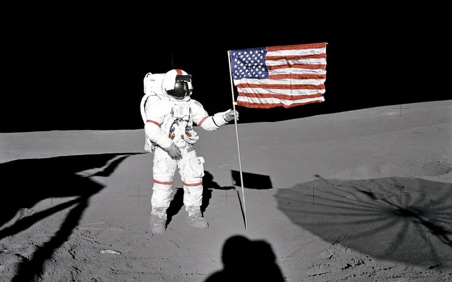 Astronaut Alan Shepard, commander of Apollo 14, standing beside the US flag on the grey lunar surface of the Fra Mauro highlands in February 1971