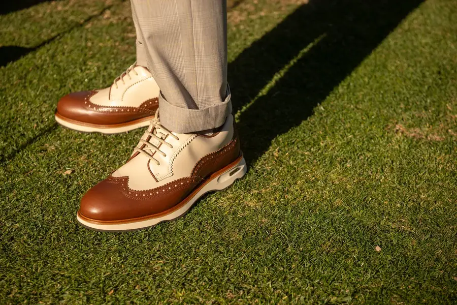 Brown and cream Lambda spikeless wingtip leather golf shoes on the grass
